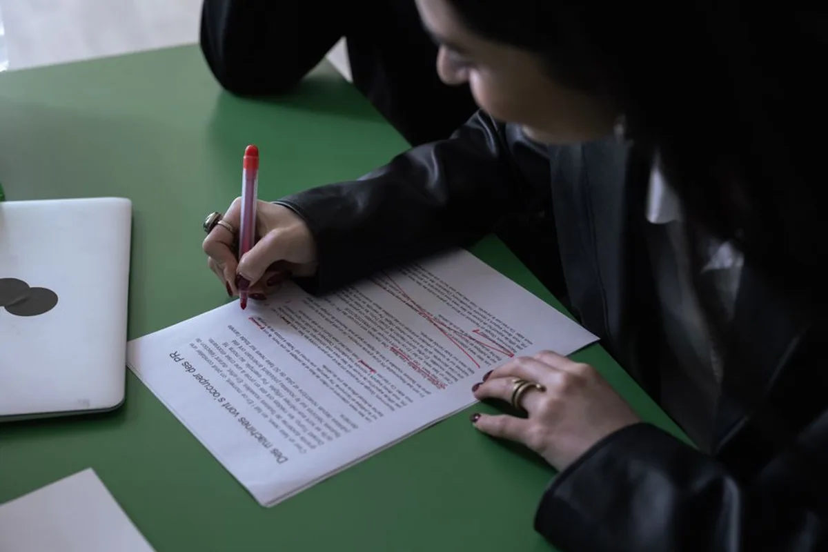 A hand edits printed text with a red pen, human review over machine-produced content