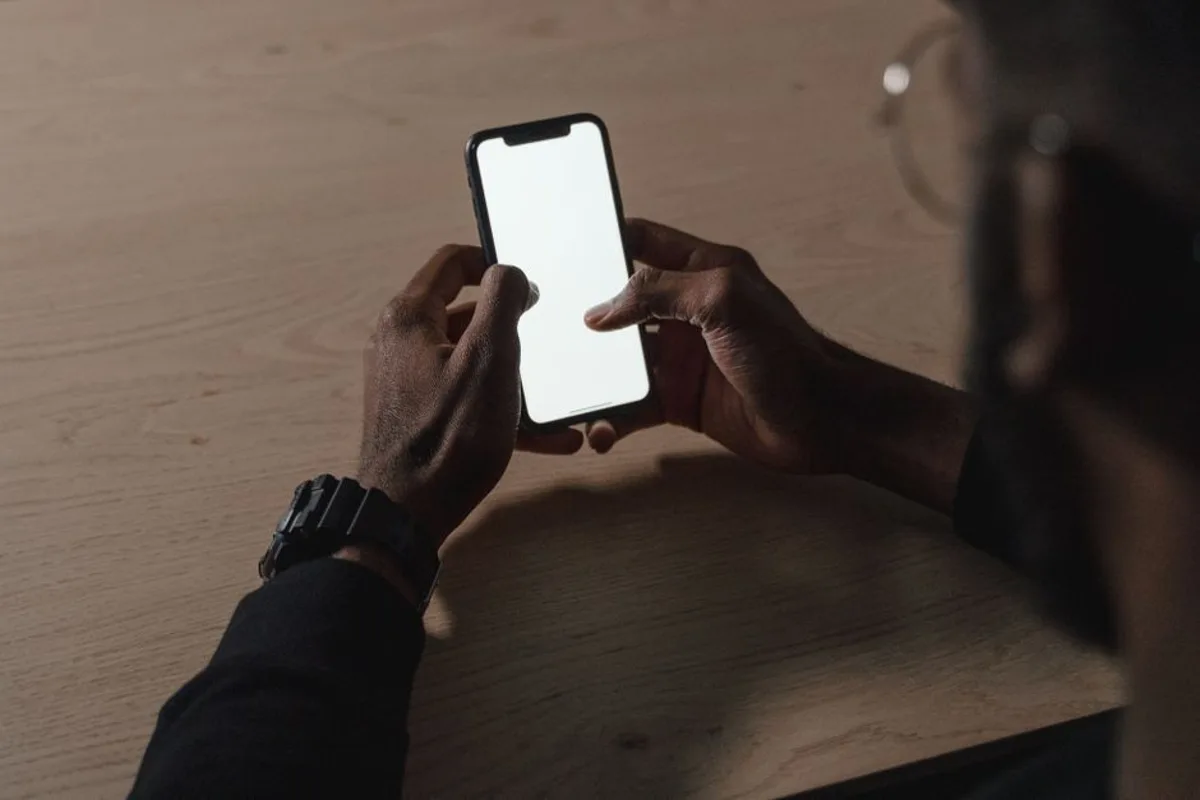Mano sosteniendo un smartphone con el pulgar en la pantalla, uso móvil con una mano