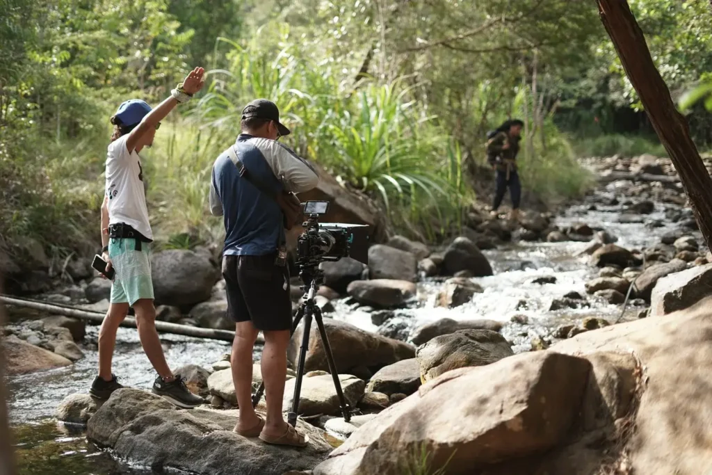 Équipe de tournage filmant en extérieur sur un terrain rocheux au bord d'une rivière